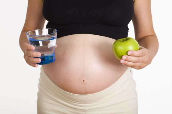 Беременная женщина со стаканом воды и яблоком в руках