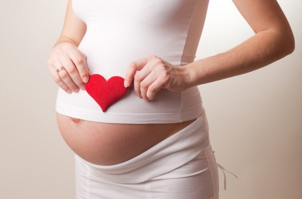 Беременная женщина держит сердечко в руках
