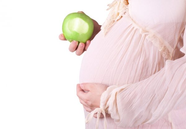 Беременная девушка держит в руке зелёное яблоко